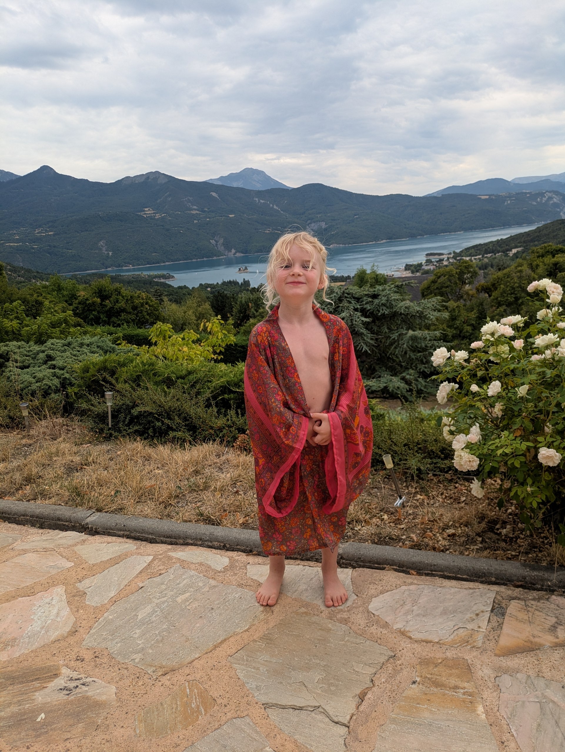 Kimono enfant imprimé fleurs sauvages corail, porté face à un lac de montagne