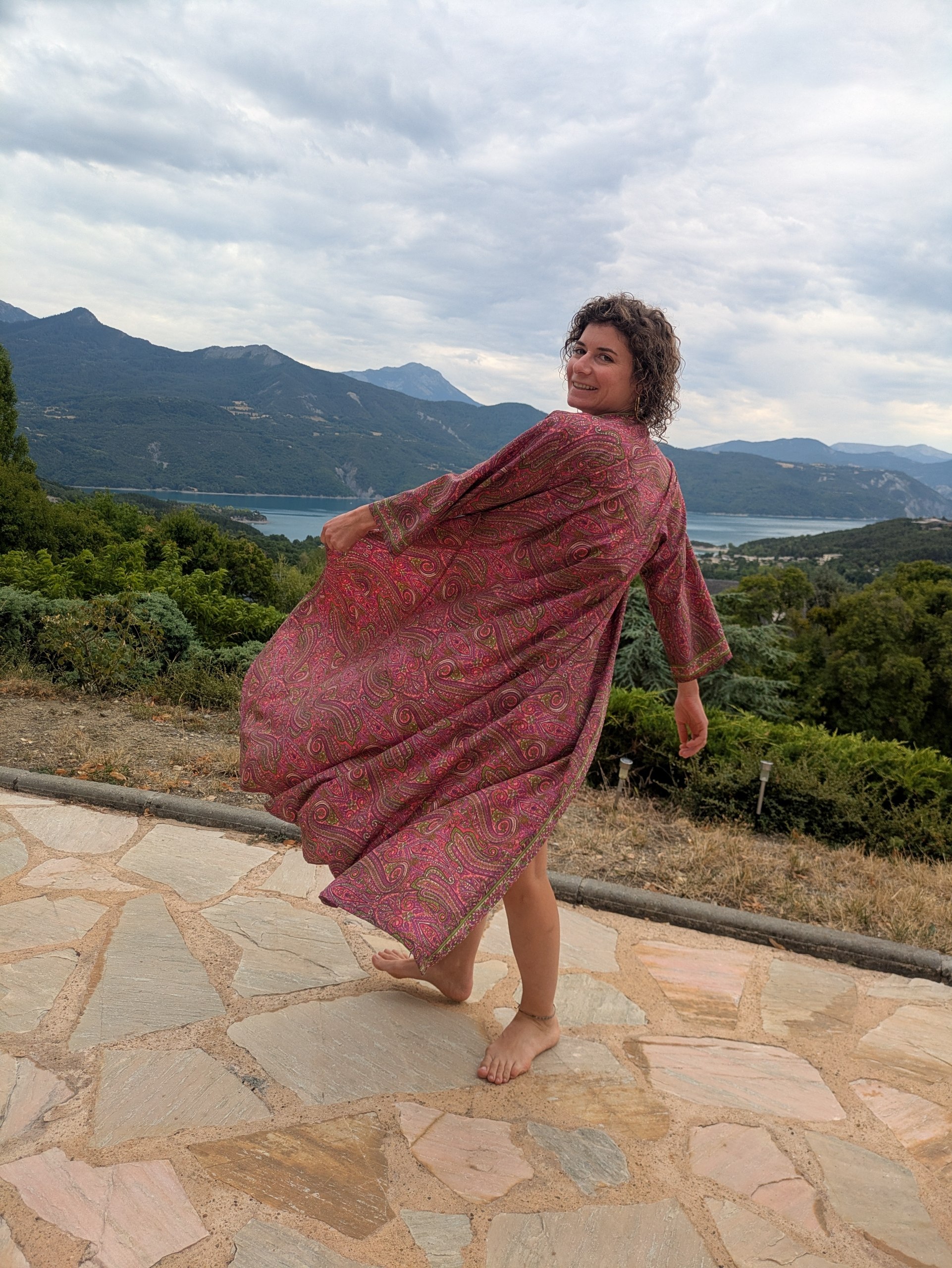 Kimono long paisley rose des sables, en mouvement face à un lac de montagne