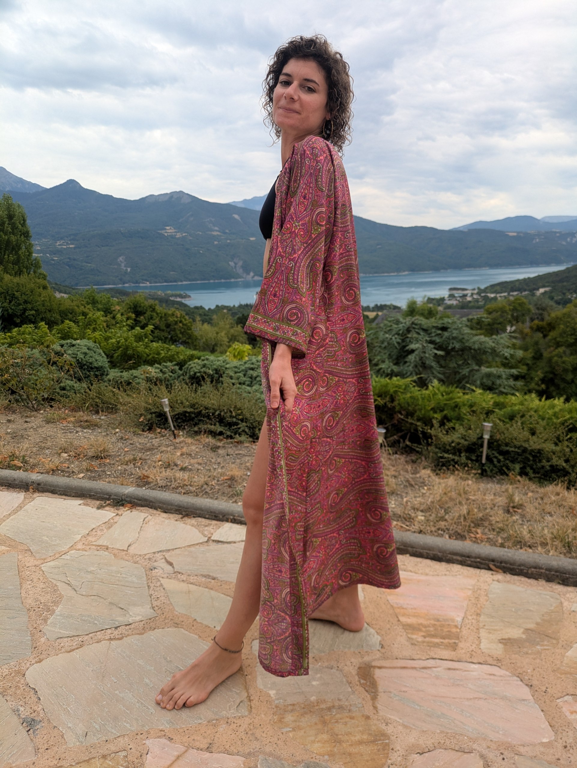 Kimono long paisley fuchsia fendu, porté face à un lac de montagne