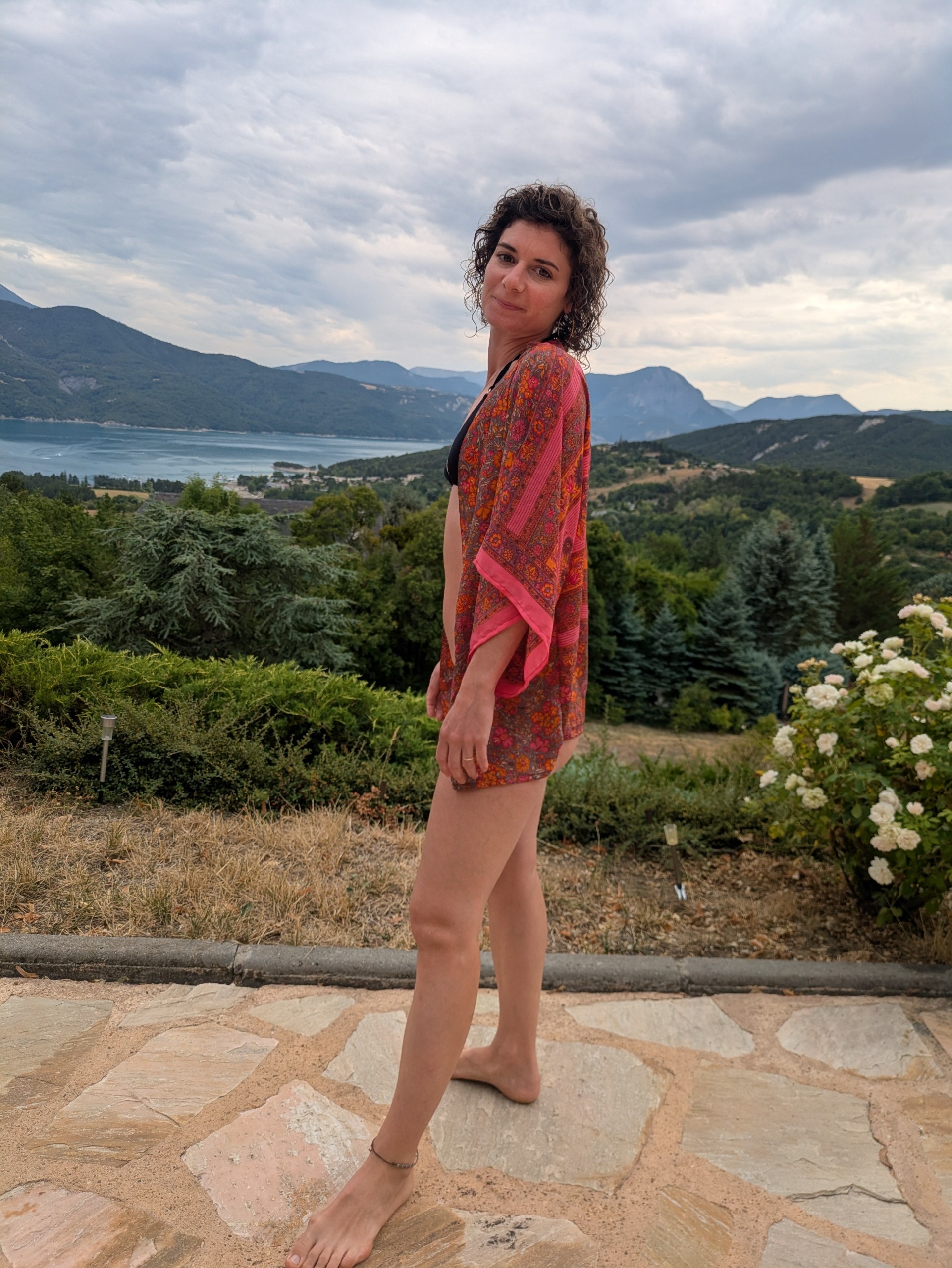Kimono court fleurs d'été corail et rose, porté face à un lac de montagne