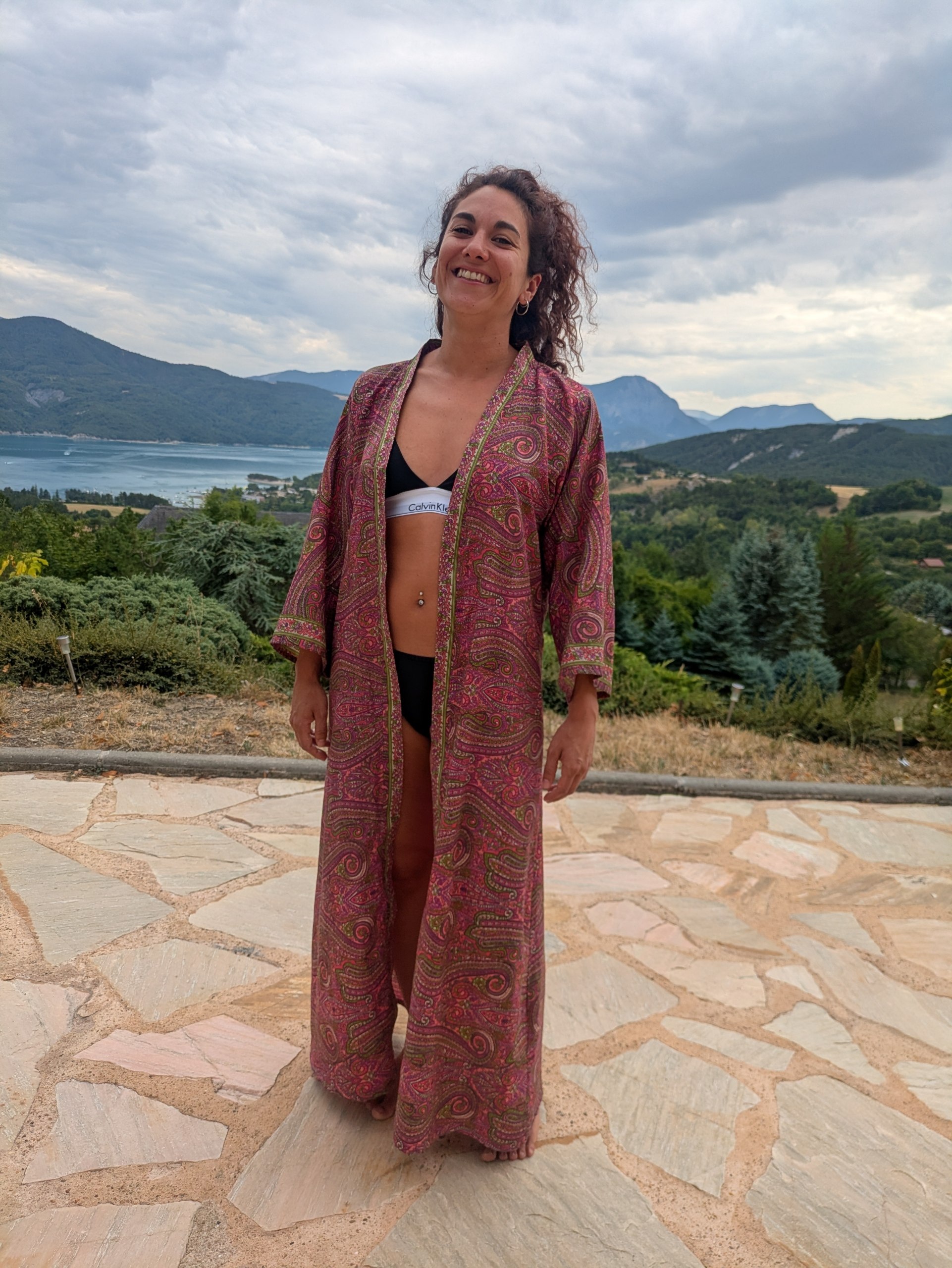 Kimono long paisley fuchsia, porté avec un grand sourire face à un lac de montagne